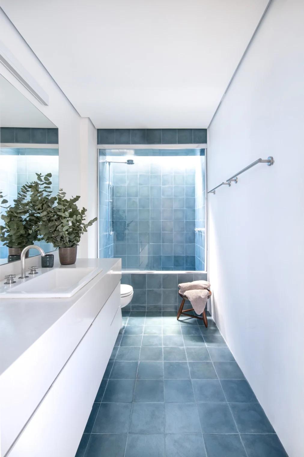 Projeto de banheiro com piso e área do box revestidos em ladrilho hidráulico azul, bancada branca minimalista e box com iluminação natural por claraboia.
