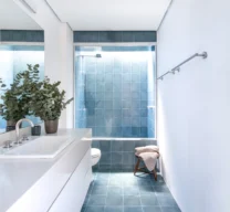 Projeto de banheiro com piso e área do box revestidos em ladrilho hidráulico azul, bancada branca minimalista e box com iluminação natural por claraboia.