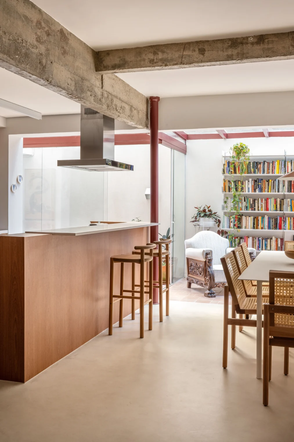 Texto Alternativo: Projeto de cozinha e sala de jantar integradas com ilha de madeira, vigas de concreto aparente no teto, piso monolítico claro e mesa com cadeiras de palhinha.
