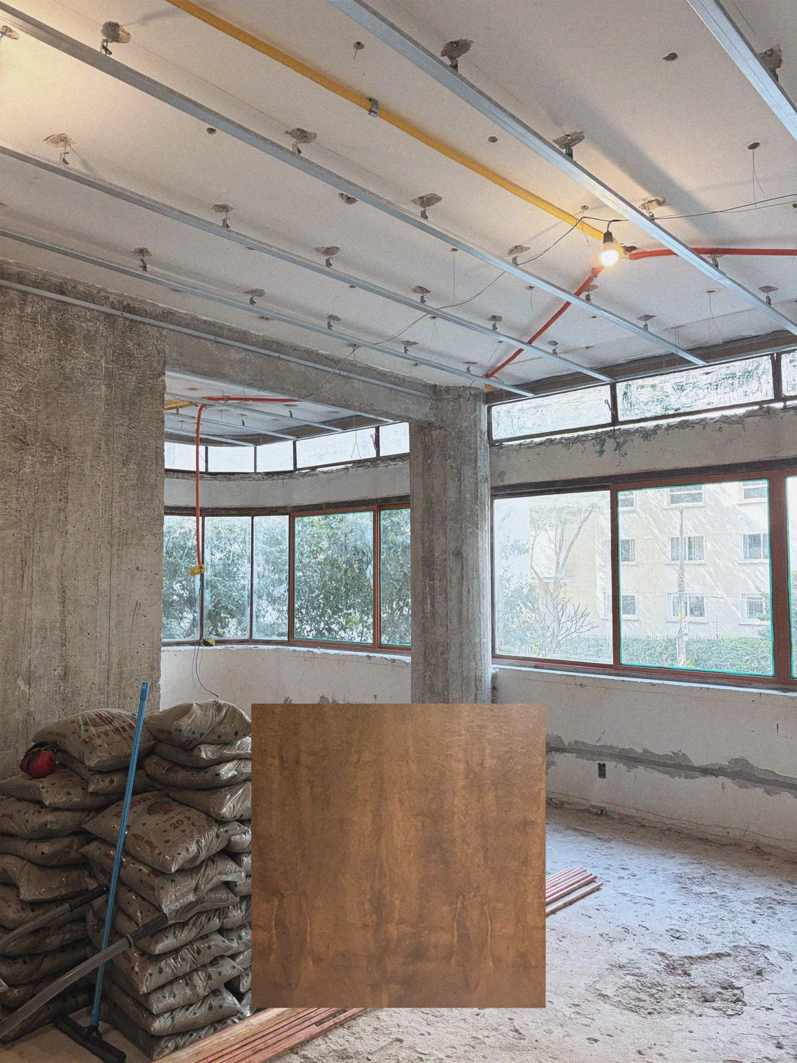 Fotografia de obra da sala em reforma no Apartamento Itacolomi com pilares de concreto aparente e perfis metálicos no teto, sobreposta por amostra de lâmina de madeira.