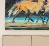 Detalhe de aparador suspenso em serralheria de chapa de aço com pintura creme, instalado sob uma tela com pintura de lobos-guará.