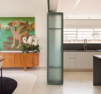 Transição entre sala de jantar e cozinha divididas por painel de correr em serralheria verde com vidro aramado, sobre piso em granilite claro.