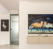 Hall com aparador suspenso creme em serralheria sob quadro de lobos-guará, porta em serralheria verde com vidro aramado ao fundo e piso em granilite claro com tapete listrado.