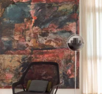 Cantinho com poltrona preta em tela, luminária de piso metálica esférica e grande quadro abstrato em tons de vermelho e escuros sobre piso de granilite claro.