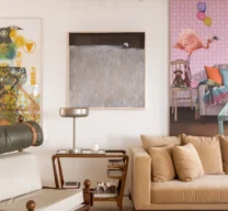 Canto esquerdo da sala de estar com poltrona Tonico em madeira e couro, carrinho de chá em madeira como mesa lateral e composição de quadros ao fundo.