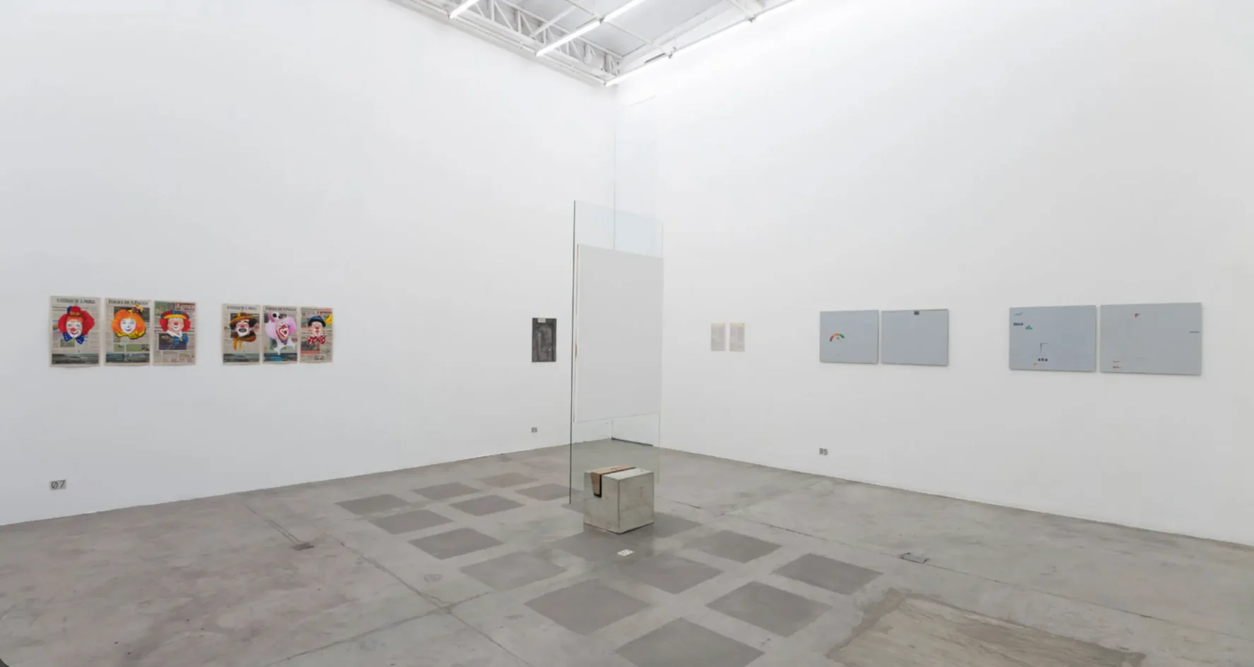 Sala de exposição com pé-direito alto na Galeria Vermelho, exibindo cavalete de vidro da Lina Bo Bardi e paredes brancas com obras de arte contemporânea.