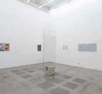 Sala de exposição com pé-direito alto na Galeria Vermelho, exibindo cavalete de vidro da Lina Bo Bardi e paredes brancas com obras de arte contemporânea.