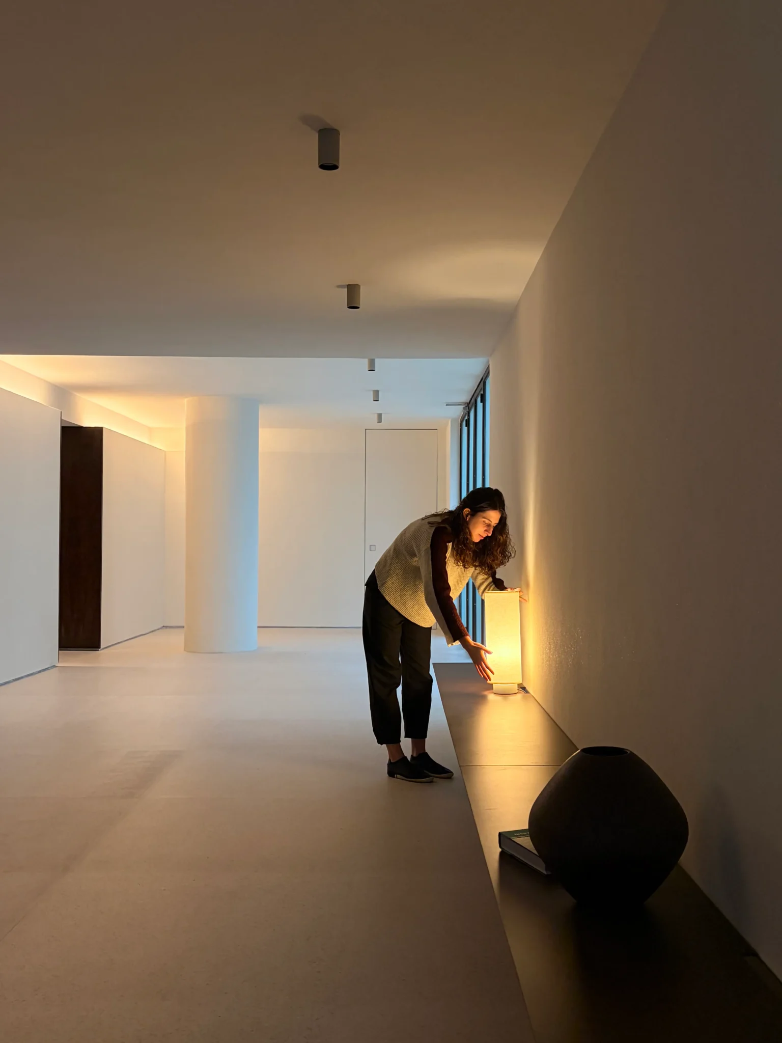 Arquiteta Marina Secaf ajustando luminária de mesa acesa sobre bancada baixa no projeto de montagem do lobby Flor de Liz.